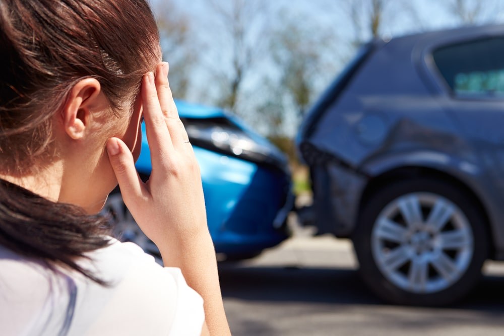 Woman holding her head as her car is towed away from a car accident.
