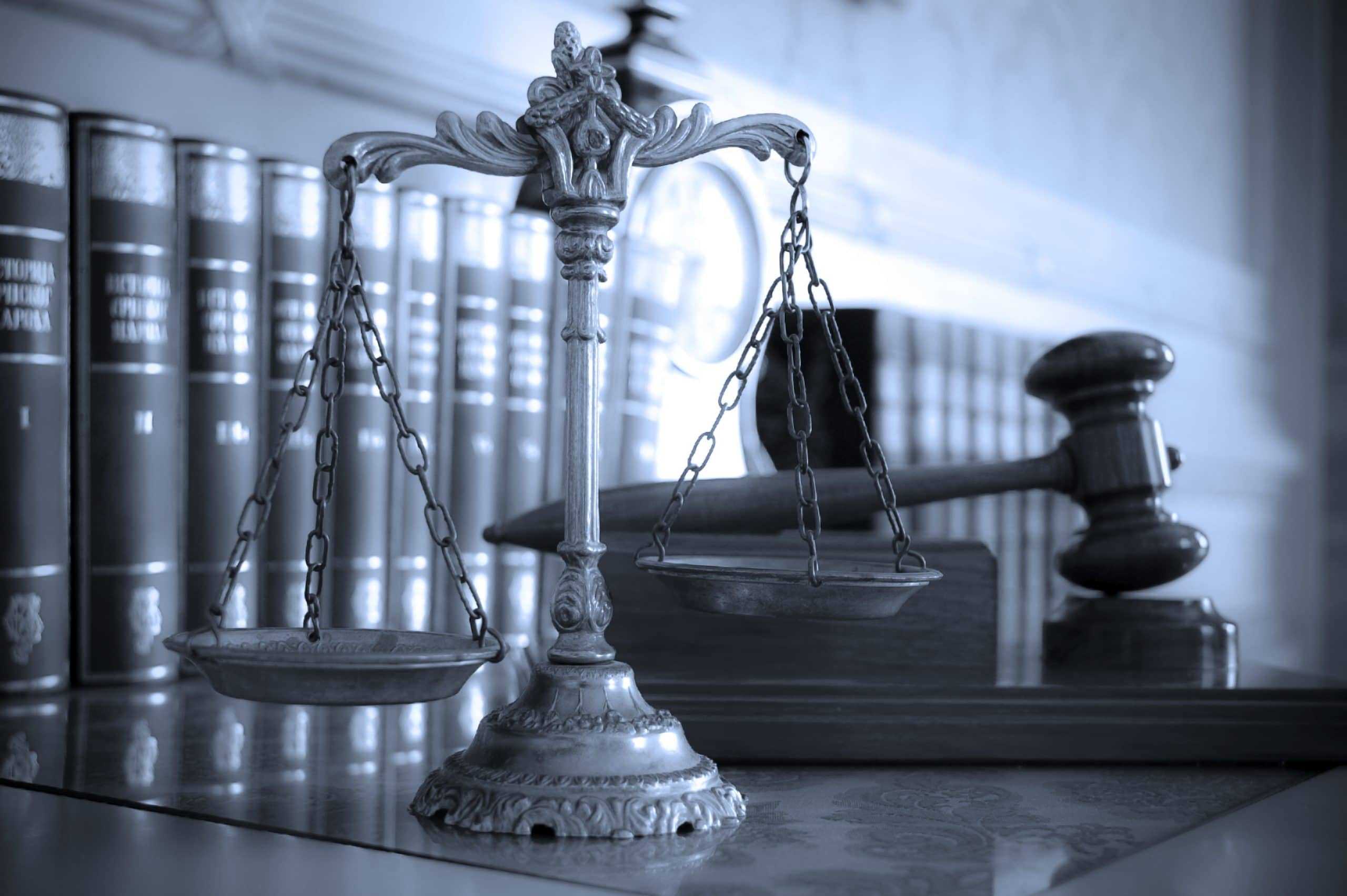 Scale of justice next to a gavel on a desk with legal books.
