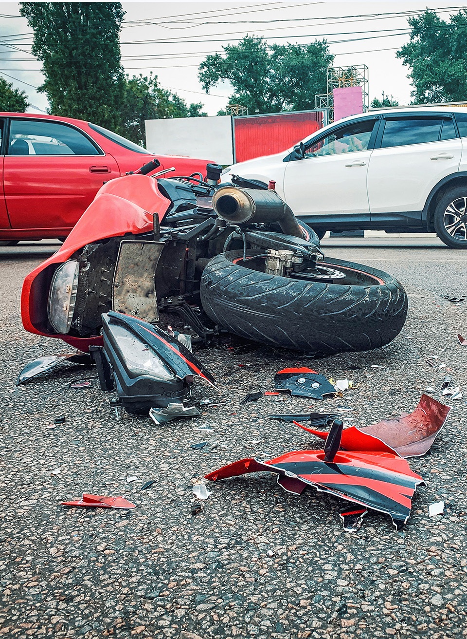 A red crashed motorcycle on its side in the street with pieces of it strewn about.